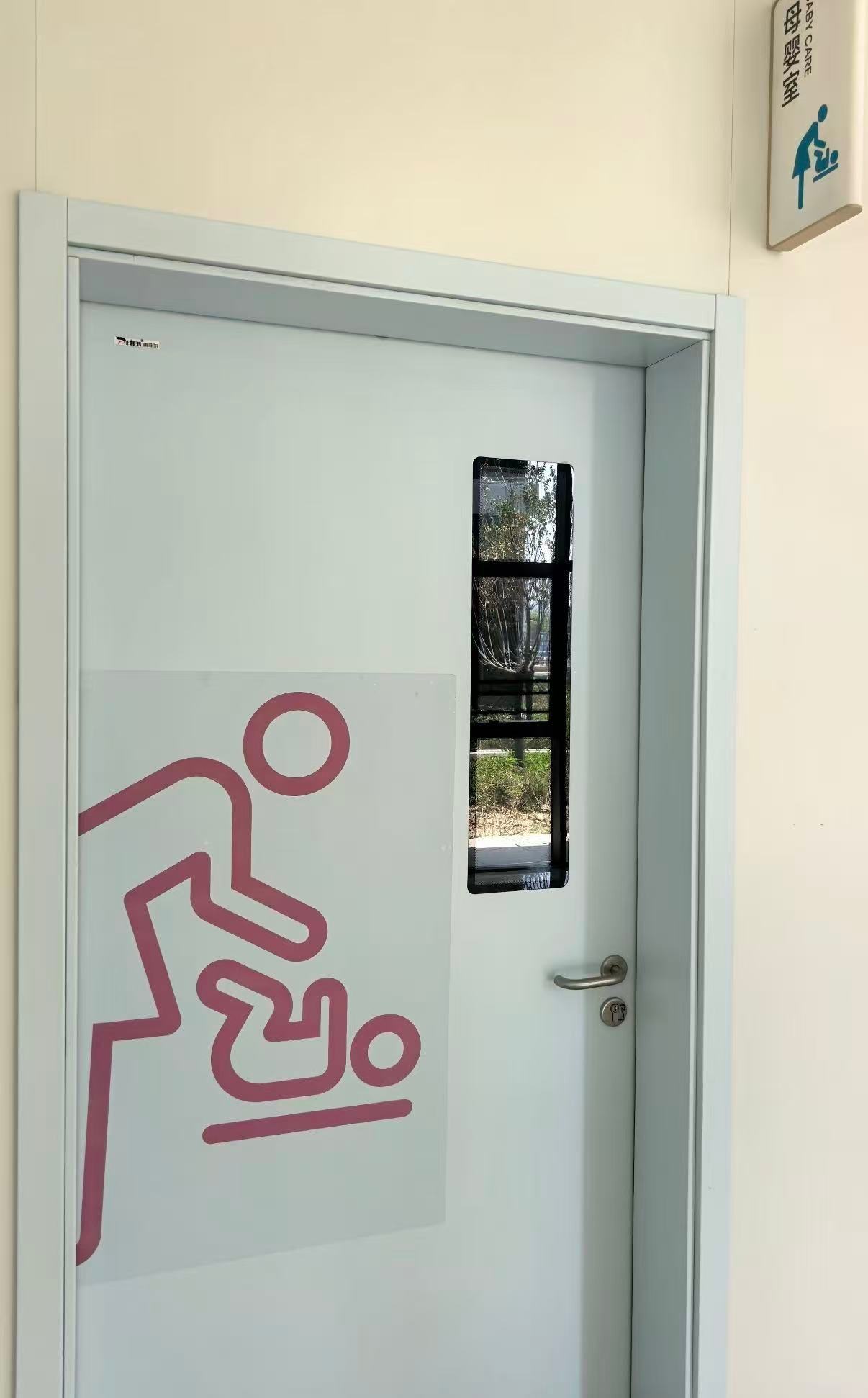 The door of a baby-care room with a glass panel and a pictogram.