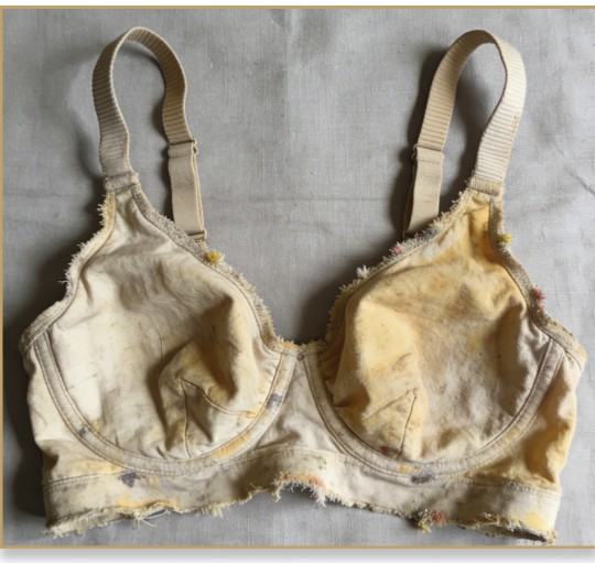 An old, stained, and fraying underwire bra laid flat.