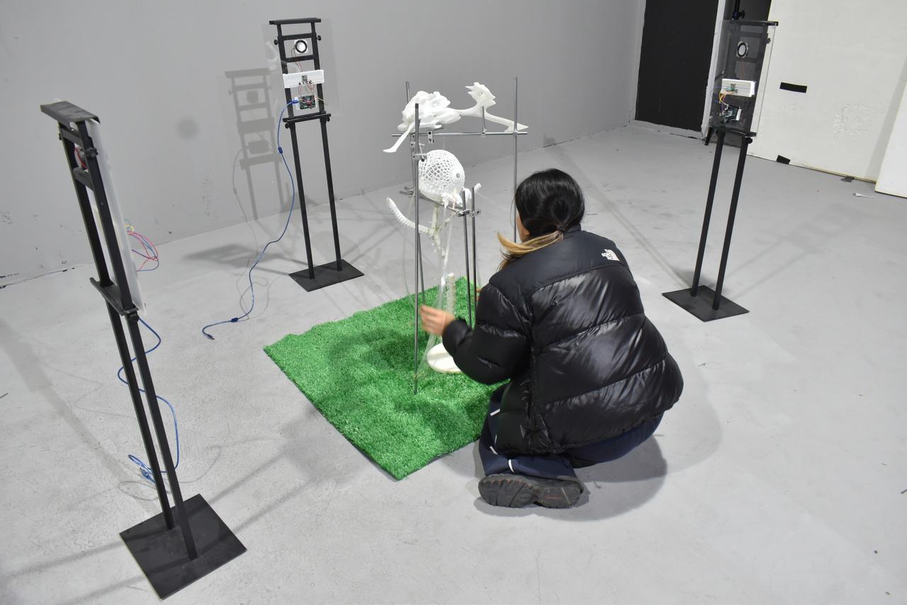 A person kneeling on a square of artificial grass, adjusting the base of the installation.