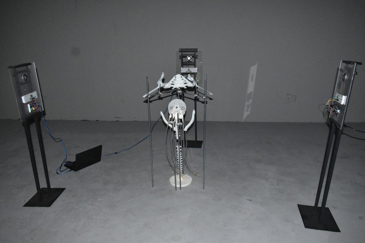Wide view of the installation with a speaker stand on each side, in a gray room.